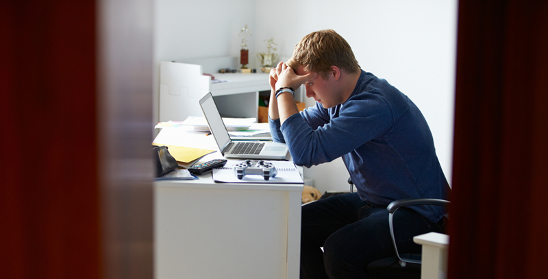 A teenage, look looks worriedly at his computer with his hands on his head. 