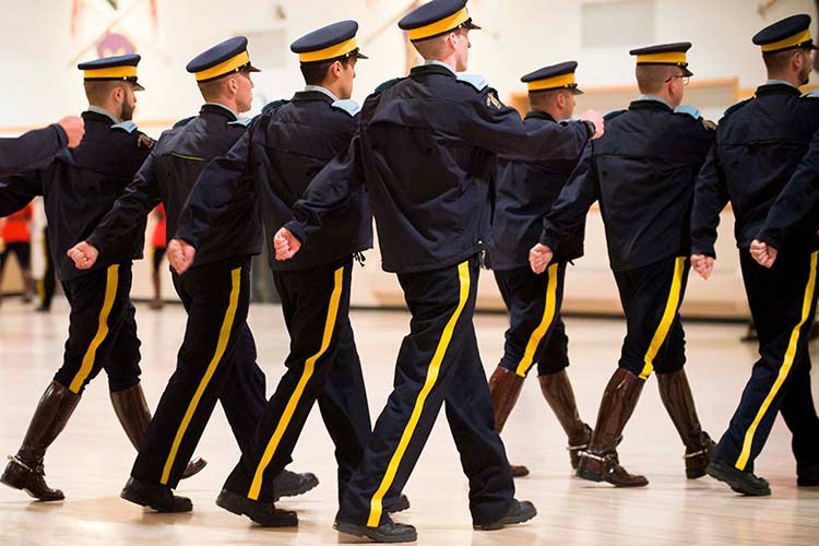 Des cadets marchent en pantalons bleus à galons jaunes.