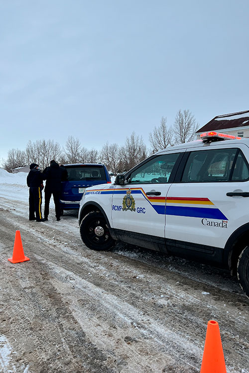 Un policier de la GRC aide une personne. Une voiture de police est à côté d’une minifourgonnette bleue.