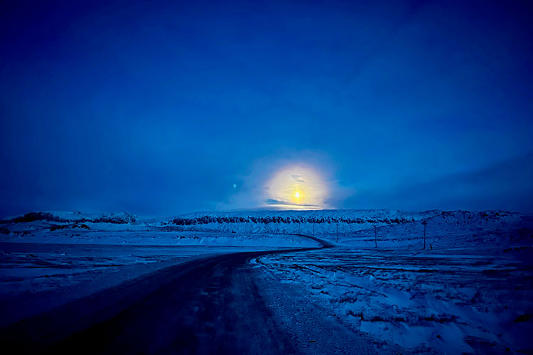 The sun rises over a snowy road on a dark December afternoon