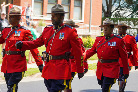 Five RCMP officers are marching down a road in red serge.