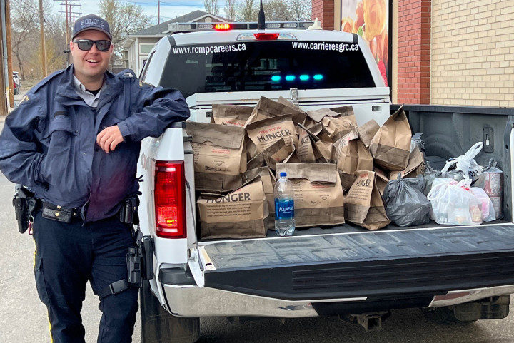 one RCMP officers standing beside RCMP truck with food donations in support of the Kindersley & District Food Bank filling the truck box