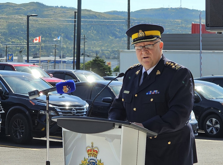 A RCMP officer in a blue serge uniform stands outside at a podium.