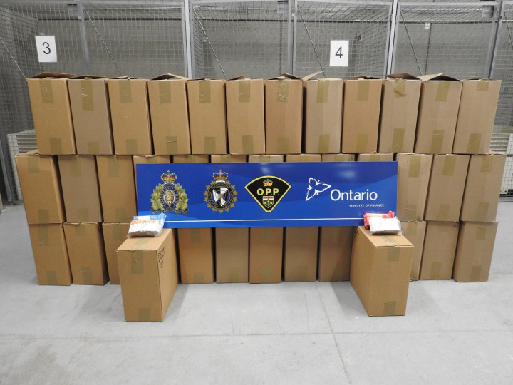 Photo of 40 boxes of unstamped cigarettes that were recovered after a suspicious vehicle stop and further investigation by CRTF. A blue placard rests on top of the boxes which includes the crest of RCMP, CBSA, OPP and Ontario Ministry of Finance. 