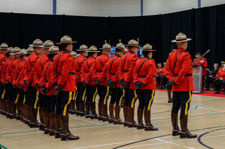 A group of RCMP officers dressed in red serge stand in two lines inside a gymnasium.