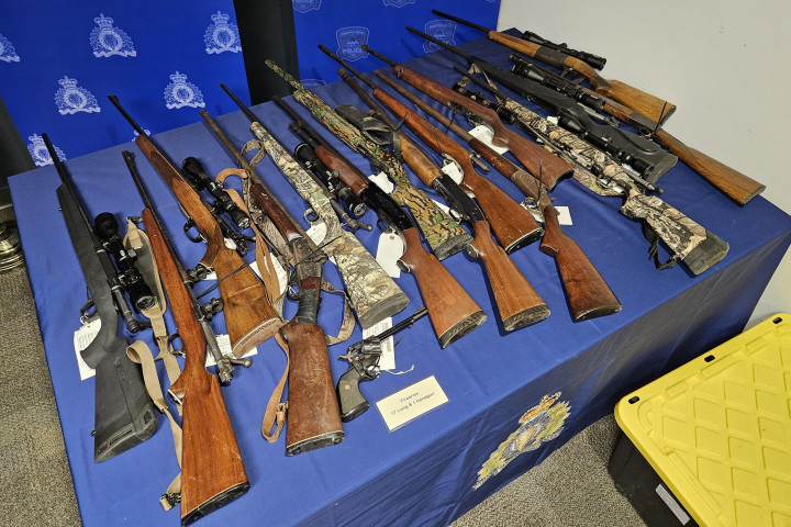 firearms that were seized during the search warrant executions are arranged on a table that has been covered with a blue RCMP table cloth