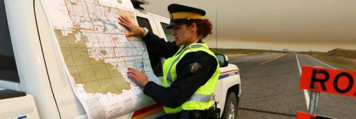 Une policière étudie une carte à côté d'une voiture de police stationnée en bordure d'une route.